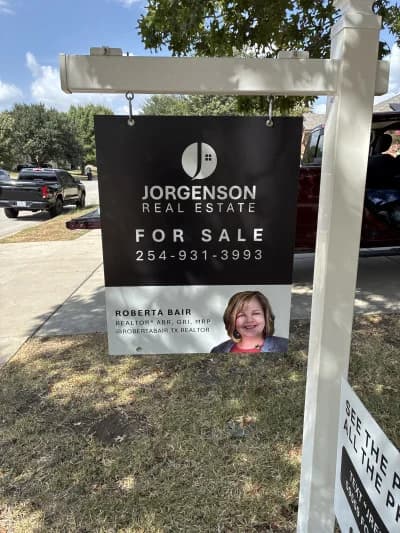 A custom Jorgenson Real Estate for-sale sign with the agent's phone number under For Sale and her headshot, name, designations, and social handle in the bottom panel